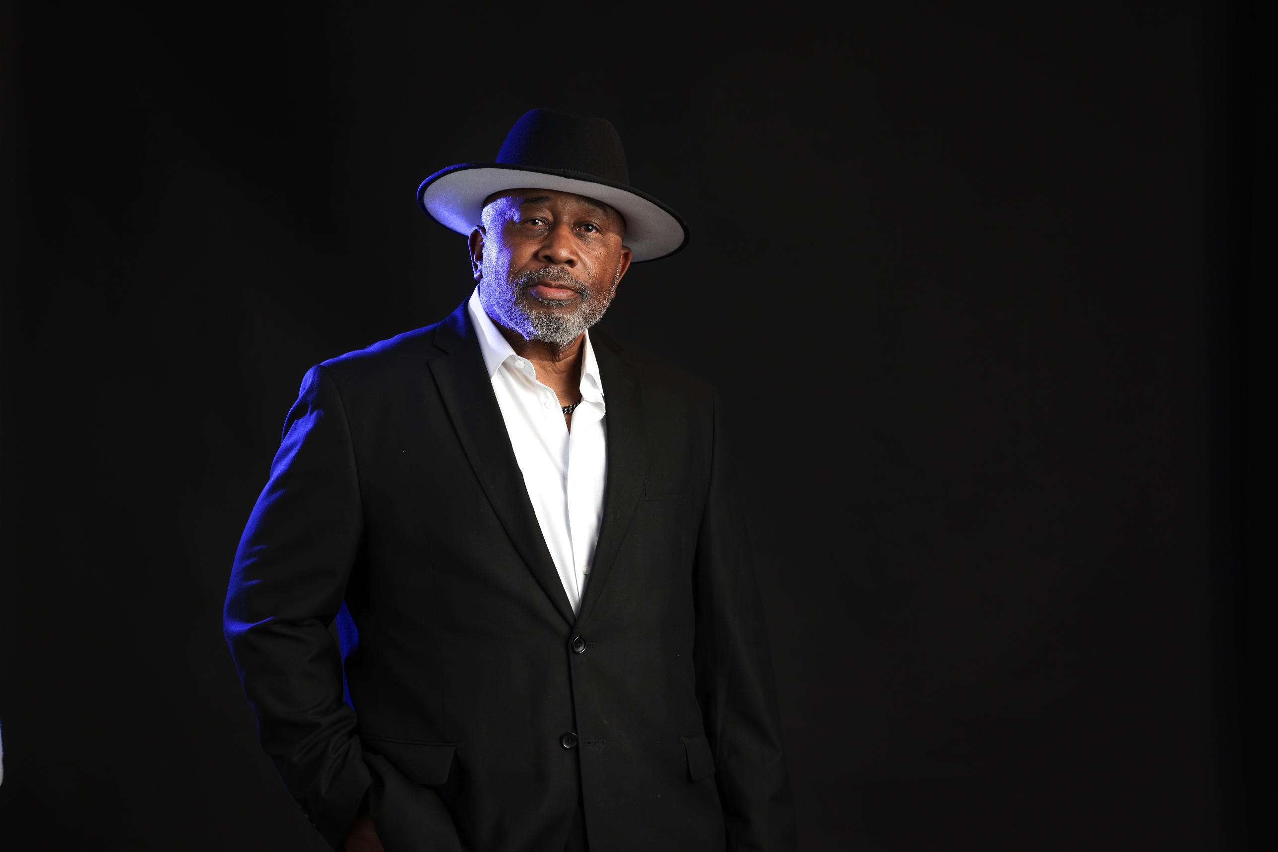James E. Alexander in a black suit and white brimmed hat, lit in blue against a dark background